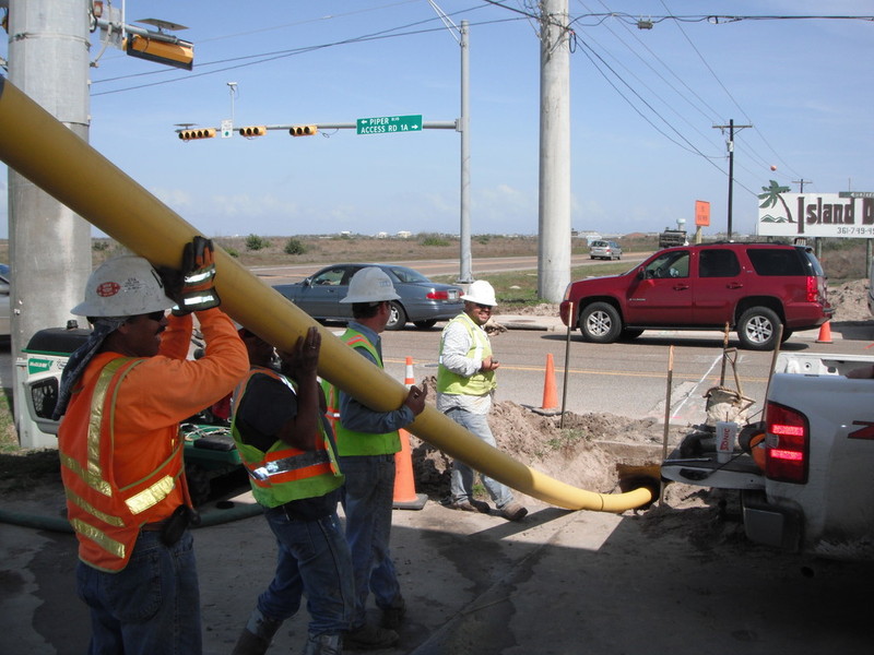 Workers manouver a plastic pipe beneath a roadway